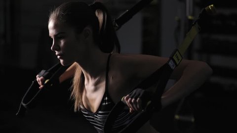 Beautiful woman doing exercise with trx straps in dark gym