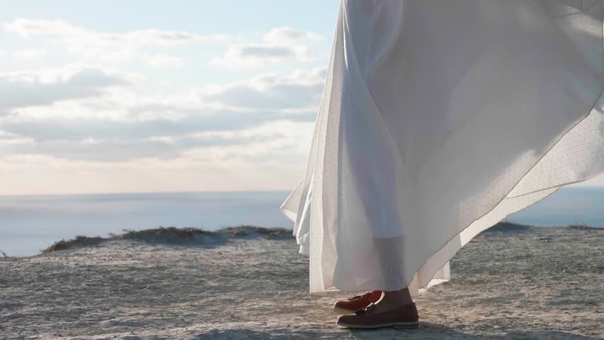 Smiling asian young woman in white dress is spinning around on the cliff with beautiful landscape on the background, slow motion. Nature, summer holidays, vacation and people concept