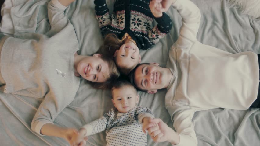 Portrait of an caucasian family with two children, happy and smiling on the bed. They are looking at camera The smiling parents are holding their two children Royalty-Free Stock Footage #1020322750