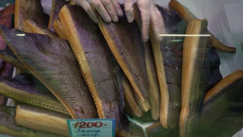 Close-up female seller hands puts smoked salted Greenland halibut in shop window at fish shop to ensure quality and goodness of food product. Concept: Asian cuisine, delicious food, fish market.