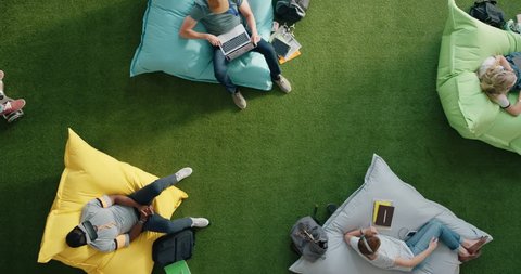 young diverse business people enjoying recreation activity in trendy office workplace sitting on colorful pillows colleague riding gyro scooter overhead