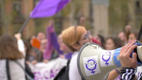 Barcelona, Spain. November 25th 2018: Megaphone Close Up with feminist stickers. Defocused women on the frame with arms up and jumping. Feminist Activists in a Demonstration. March