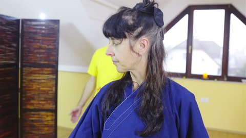 Woman in kimono showing learner of shaolin forms indoors HD. Portrait crane shot of person in focus showing martial art form and man in background out of focus repeating.