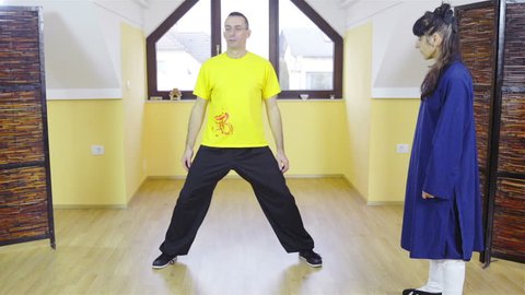 Shaolin teacher correcting learner when making martial arts forms HD. Static shot of male person in yellow shirt in focus and exercise martial arts forms while teacher stand in right part of frame.