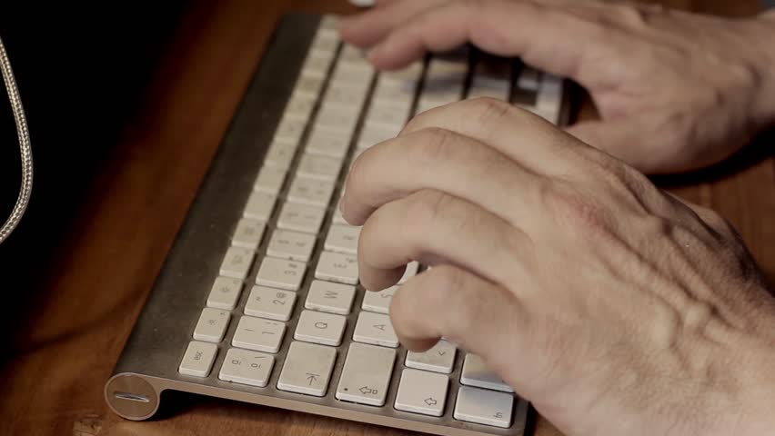 Male Hands typing on Wireless White Mac Keyboard at Wood Table. Closeup.
