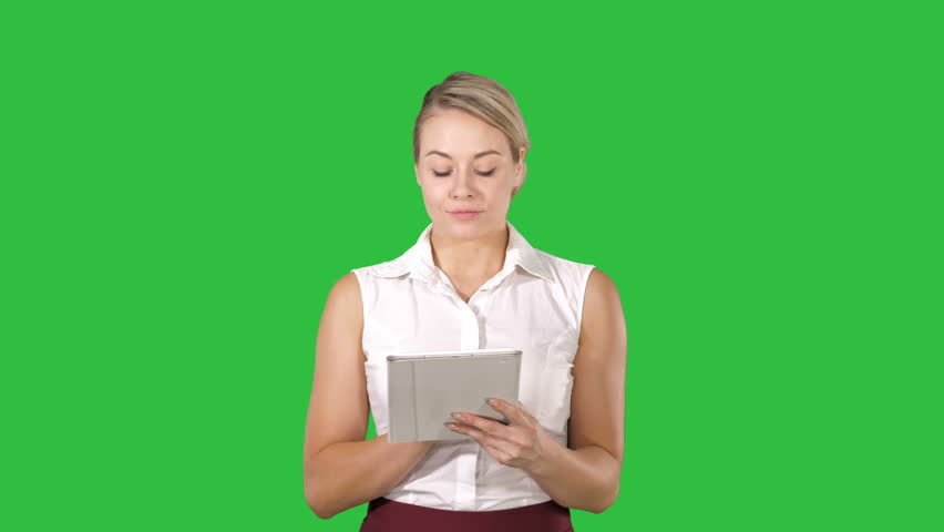 Beautiful girl holding a tablet touch pad computer gadget swiping pages and looking in camera on a Green Screen, Chroma Key.