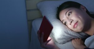 Woman watch on video on cellphone at night time and lying on bed