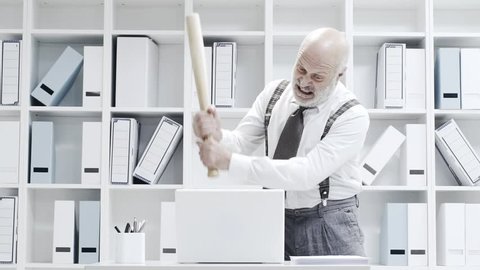 Stressed crazy businessman smashing his laptop in the office using a baseball bat, anger and computer problem concept