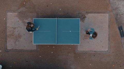 Clean and minimal top drone footage of two best friends or student young girls have fun outdoors. Play ping pong or table tennis in park playground. Laugh and smile in friendly competition game
