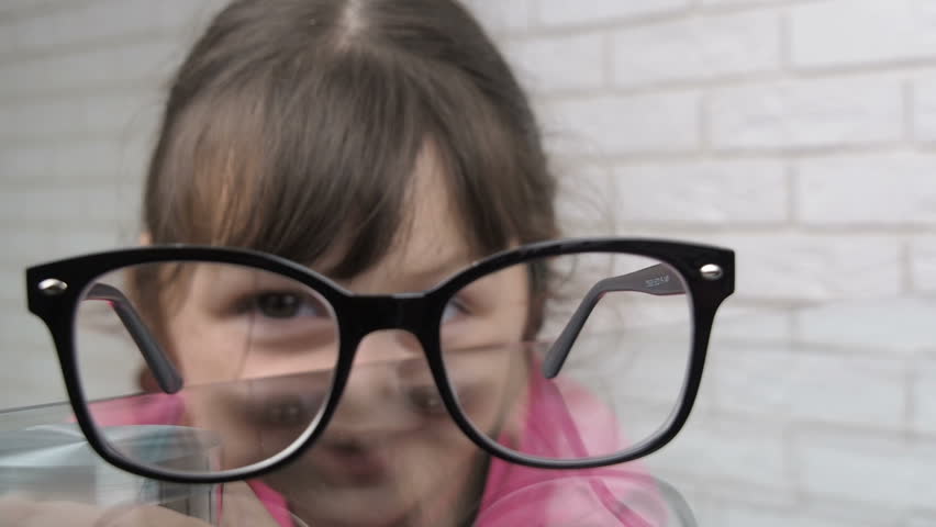 Wearing glasses. Girl with pigtails wearing her eyeglasses which was lying on the table a moment ago