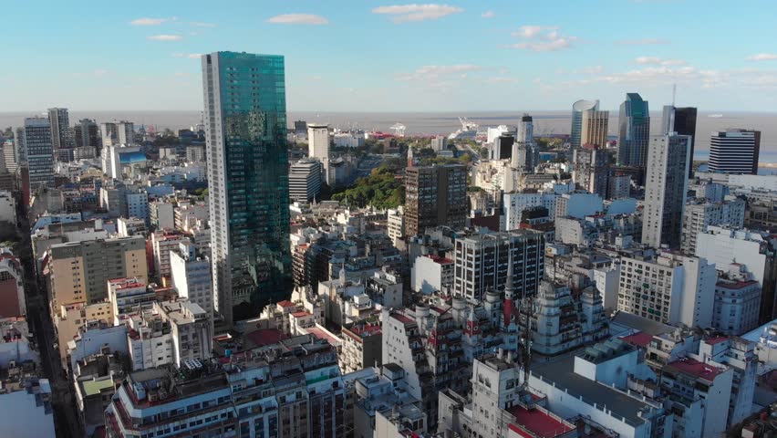 Panoramic aerial drone view of Buenos Aires city downtown in late afternoon over skyscraper buildings, cars and traffic visible in the streets below. Retiro and Plata river in background.