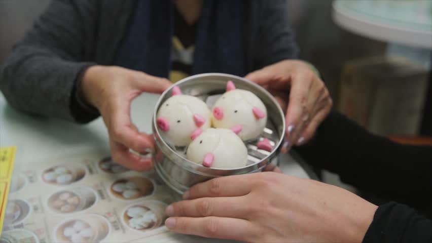 This video shows two diverse women tourists, an older asian woman and a young caucasian woman, enjoying cute pig shaped dim sum together at a restaurant in Hong Kong.