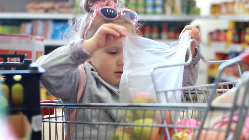 Baby at the grocery store buys fruit. Child girl siting in the grocery cart and puting the apples in the package. Royalty-Free Stock Footage #1020378865