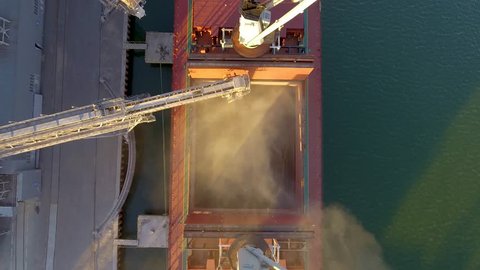 Close view of ship loading grain crops on bulk freighter via trunk to open cargo holds at silo terminal in seaport. Cereals bulk transshipment to vessel. Transportation of agricultural products.