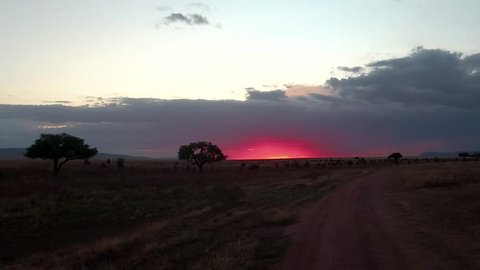 Sunset in African savannah, sun setting behind dramatic clouds in Tanzania, steady shot, wide angle