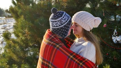 man covers his girlfriend in warm plaid and kiss while walking in cold winter park