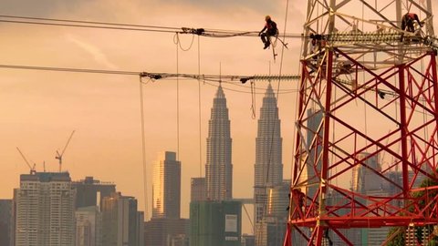 Footage of electricians in silhouette working on a new power transmission tower as part of the nation power grid in Kuala Lumpur, Malaysia. Dramatic scene. Zoom out motion.