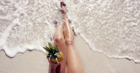 Top view of woman holding pineapple cocktail sexy legs on beach self shot
