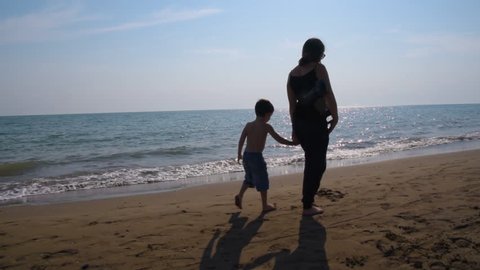 Mom and little son talk and walk on the shore of the beach