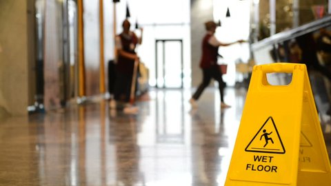 Yellow warning sign wet floor. Sign showing warning of caution wet floor and workerw cleaning hall floor of  business building.