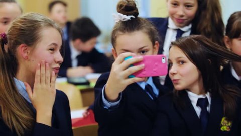 Lviv \ Ukraine - July 7 2018: Young funny girls in the uniforms having fun while taking selfie pictures on the smartphone at the school in classroom break happy education together schoolgirl pupil