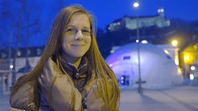 Portrait shot of Female citizen of Ljubljana city HD. Jib shot at night of attractive female person smiling in camera, big blue tent in background and castle on top of hill.