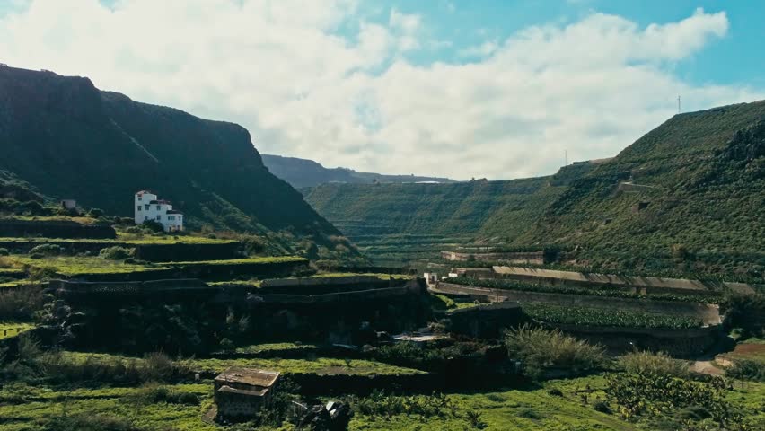 aerial drone footage of beautiful stunning landscape with fields and terraces for planting vegetables and fruits with a colonial farm house in a valley on a sunny day