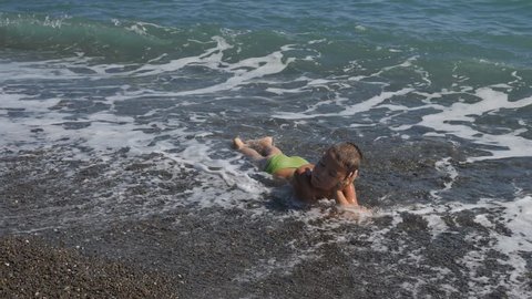 boy in the sea surf. Child covers the wave. The boy lies in the sea on the rocks. Water lulls the baby.