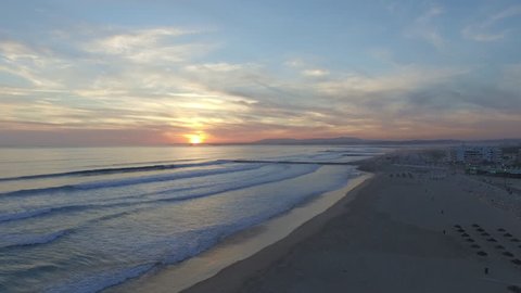 Wide horizon drone shot at Costa de Caparica with some people in the frame on the sea wall .In the horizon you can see an amazing sunset in Lisbon and some mountains of Sintra. Shot by drone