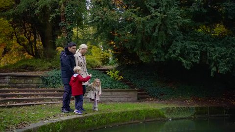 happy family is standing on edge of picturesque pond in park in autumn day, relaxing
