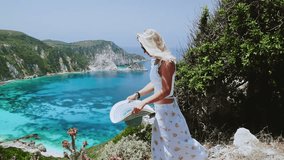 Woman putting hat on her head. Blonde posing in front of amazing scenery of Petani bay. Summer vacation lifestyle concept. 
