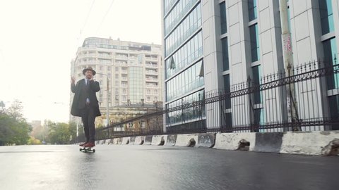 Businessman skateboarding near office center and using cell phone by business