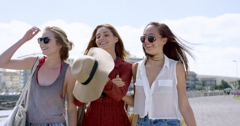 Three young women tourists on summer vacation girl friends walking on beach promenade wearing denim shorts