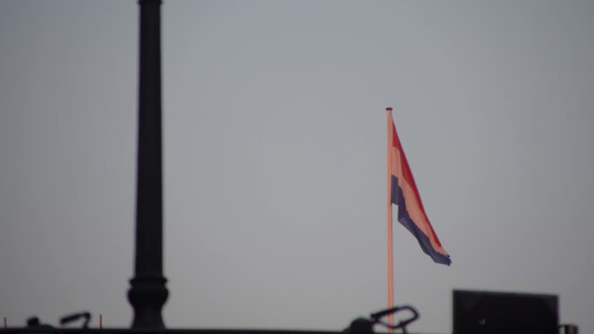 Passing under a bridge with a bicycle locked to the railing in silohuette while watching the Dutch flag of the Netherlands wave in the breeze beyond