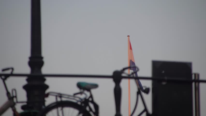 Passing under a bridge with a bicycle locked to the railing in silohuette while watching the Dutch flag of the Netherlands wave in the breeze beyond