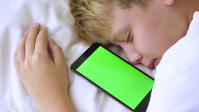 Closeup profile video portrait of cute little tired sleeping child boy holding modern smartphone with blank empty green screen. Real time 4k footage.