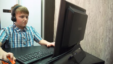 The boy plays an online game on a computer through an Internet monitor with headphones.