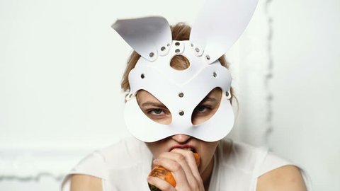 Close up of a woman in a leather mask who eats carrots. Fashion concept. BDSM concept. Hot girl in leather mask