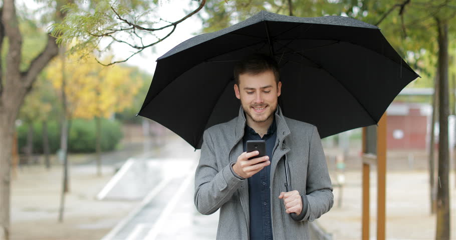 Front view portrait of a happy man talking on phone walking under the rain
