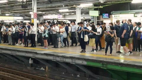 Tokyo, Japan - August 2018: Train arriving at a subway station platform while commuters wait in line