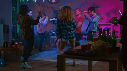 At the College House Party: Diverse Group of Friends Have Fun, Dancing and Socializing. Boys and Girls Dancing in the Circle. Disco Neon Strobe Lights Illuminating Room.