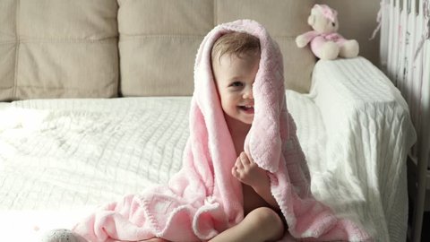 Little cute girl after bath sits playing with a towel and laughs