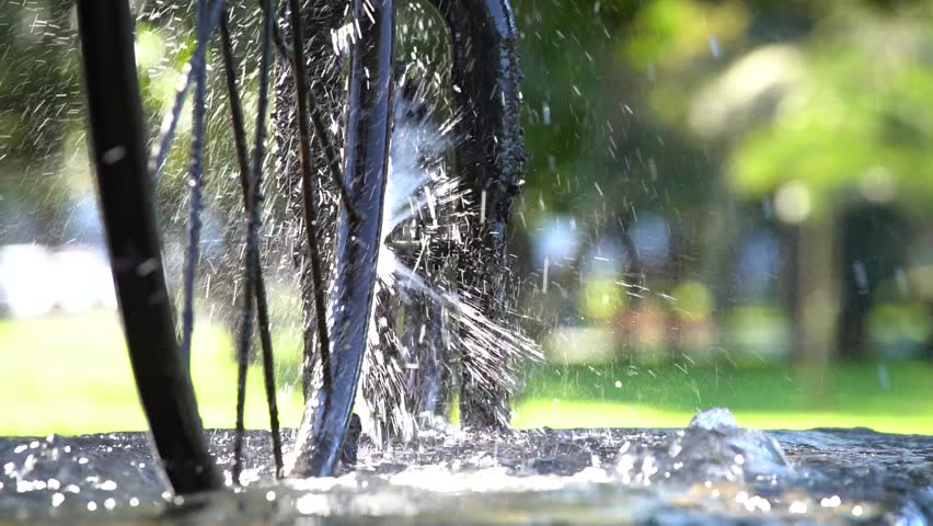 Beautiful fountain and spinning bicycle wheel against sunlight with water splashing in city Batumi on a sunny day, Georgia. Slow motion, close up