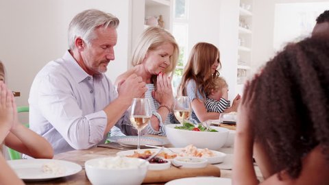 Multi-Generation Family Sitting Around Table At Home Saying Grace Before Meal