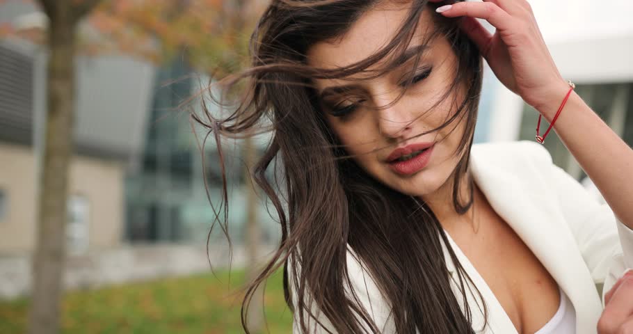 4k. Slow and fast motion. Fancy dressed young business woman in black and white clothes walks along the pass before a modern glass building, turns around, shakes her hair and looks straight into the