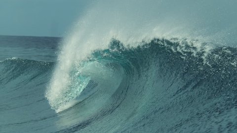 SLOW MOTION, CLOSE UP: Glassy water sparkles in the sun as tiny droplets fly away from large barrel wave coming from the vast Pacific Ocean. Beautiful deep blue ocean wave splashing near exotic island