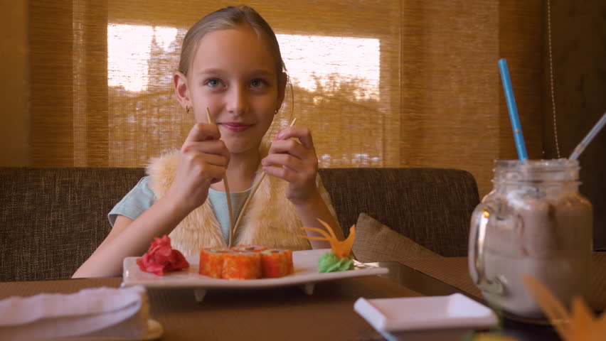 Happy teenager girl spliting chopsticks for eating sushi roll in asian restaurant