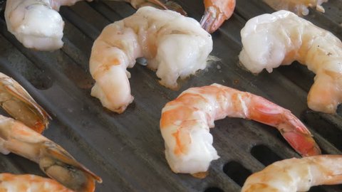 Closeup of shrimp cooking on a grill in 4k. The shellfish cooks on a searing hot cast iron grate. Authentic shot could be used in videos on cooking, travelogues, food allergies and global overfishing.