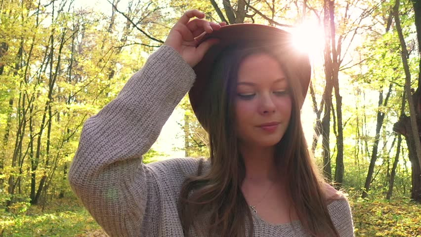 Portrait of a beautiful smiling girl in a hat with a yellow maple leaf in the foreground in the autumn forest. Slow motion