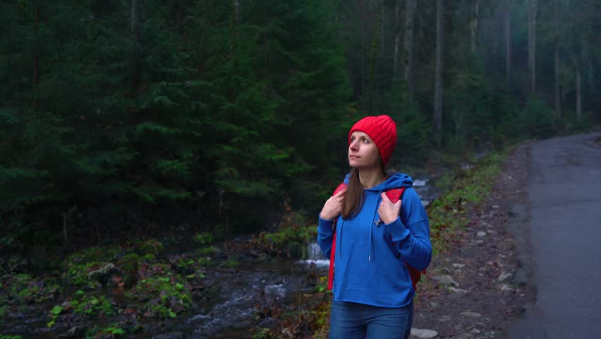 Woman traveler with a backpack walks on the road in the mountains along the river and admires the surrounding scenery